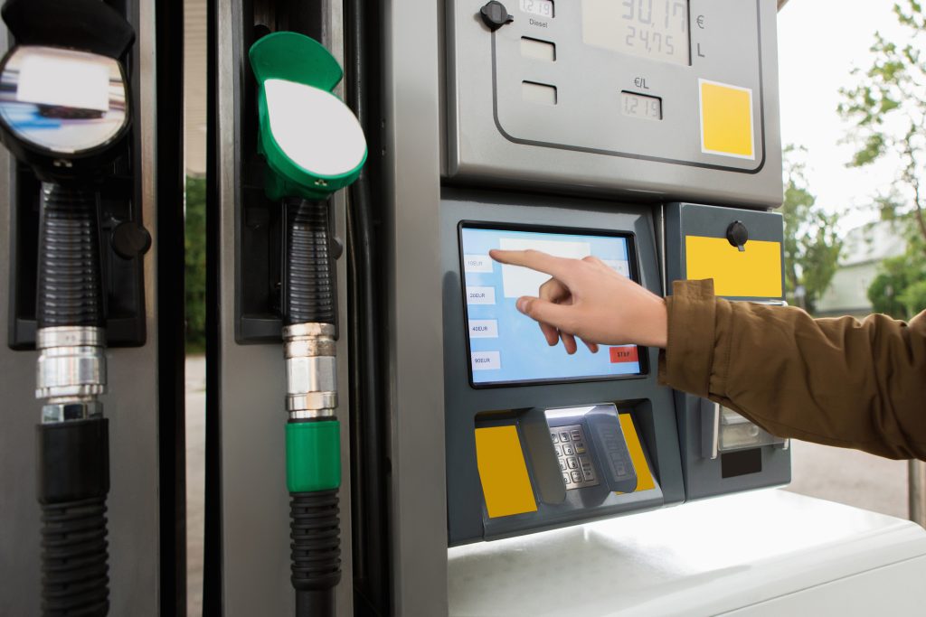 A person using a touch screen interface at a fuel pump with fuel nozzles