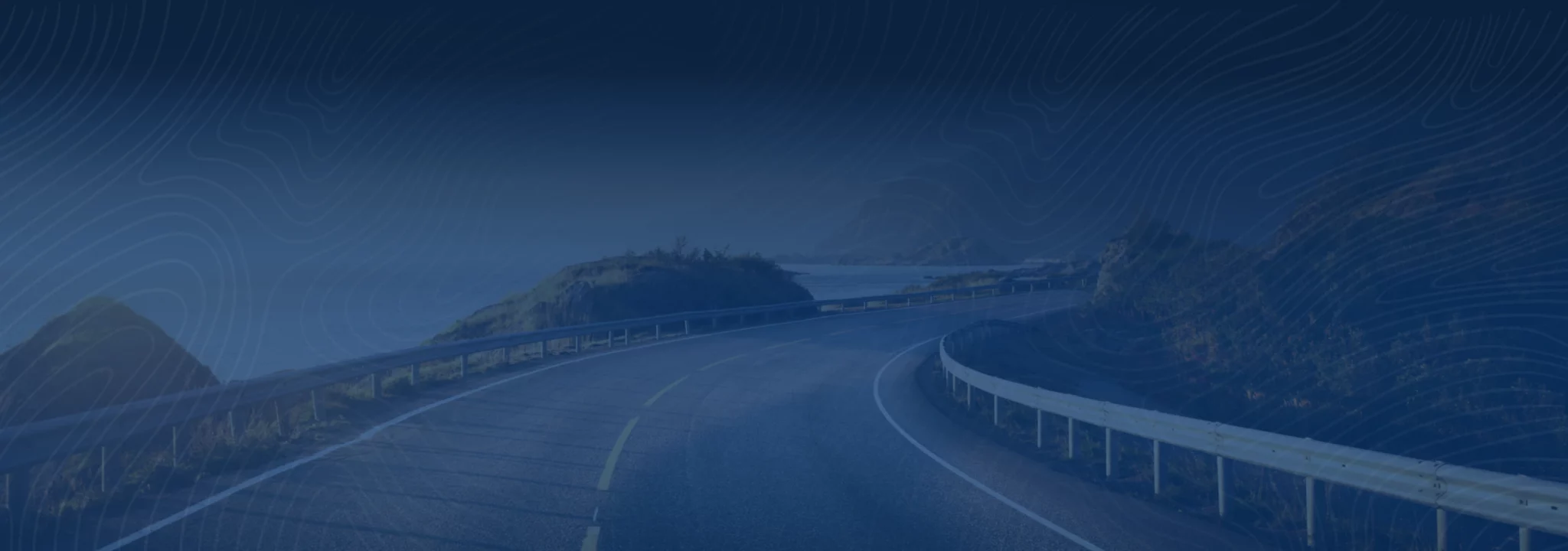 Picture of the road going along the ocean coast line. Mountains on one side of ocean are covered in lush greenery
