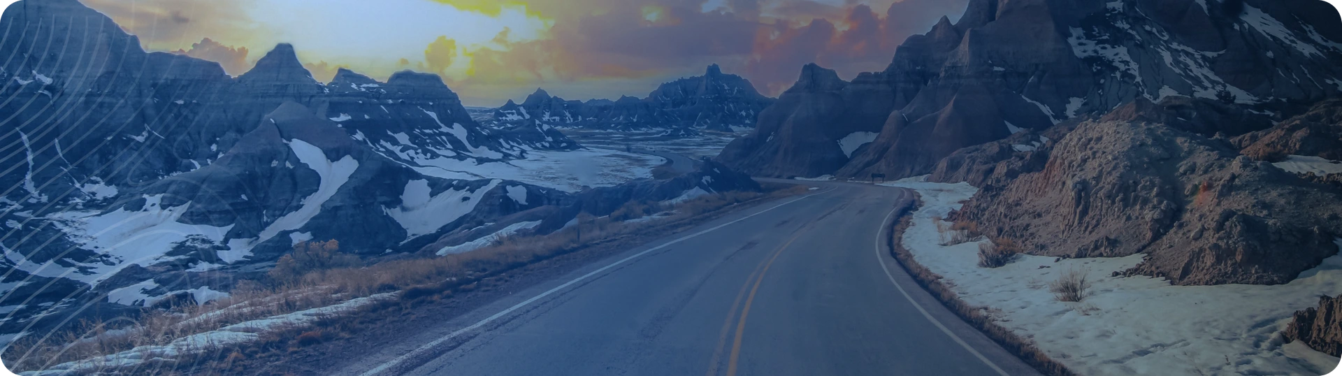 a road in the rocky mountains with snow lying on the sides and a sunset