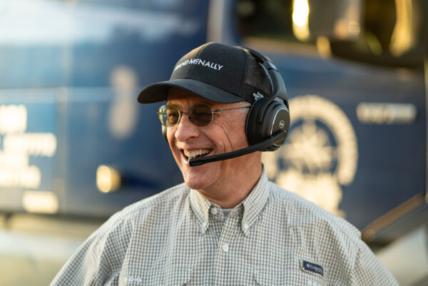 Smiling driver wearing Rand McNally ClearDryve 220 Wireless Bluetooth Headphones, showcasing hands-free communication and comfort for professional use.