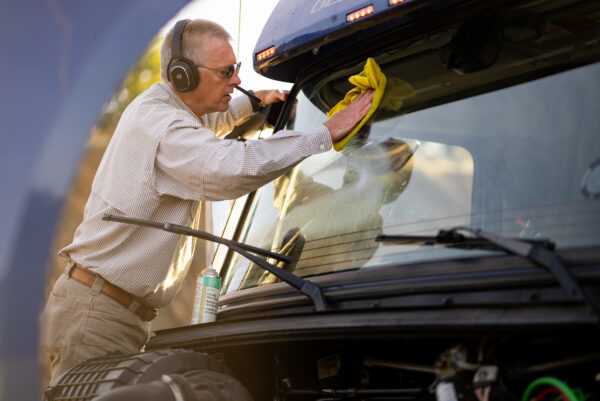 Driver wearing Rand McNally ClearDryve 220 Wireless Bluetooth Headphones while cleaning a truck windshield, highlighting hands-free functionality and convenience for professional drivers.