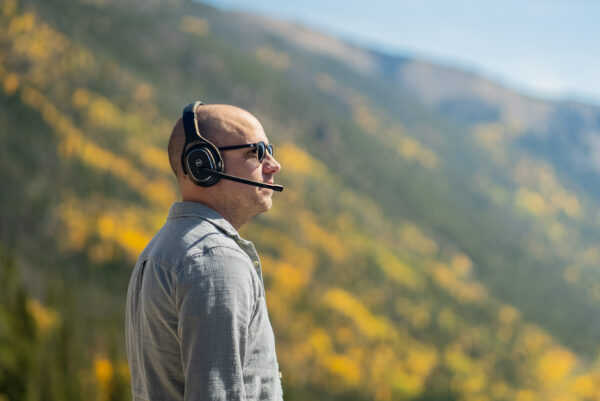 Man wearing Rand McNally ClearDryve 220 Wireless Bluetooth Headphones outdoors, with a scenic mountain background, showcasing the headphones' versatility and comfort for professional and recreational use.